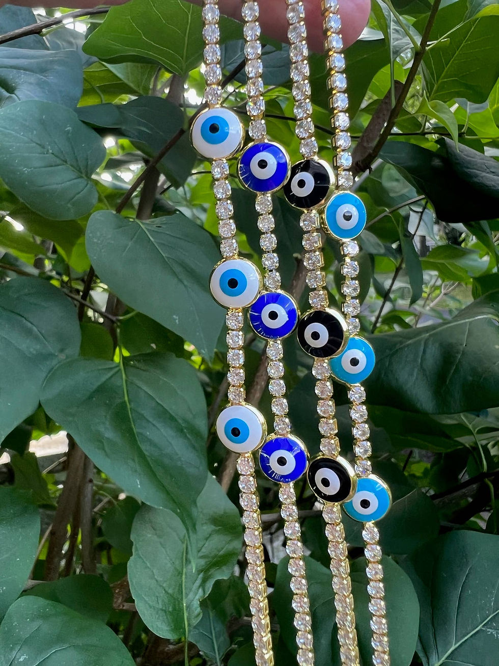 Close-up of diamond tennis bracelets with evil eye charms, green background.