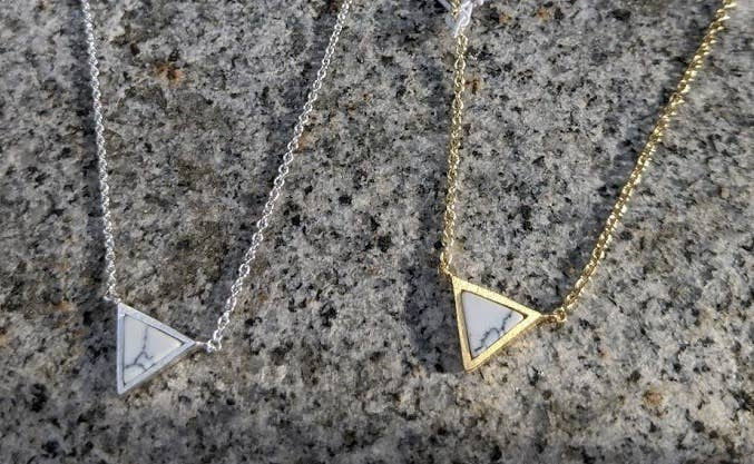 Thumbnail: Two triangle necklaces resting on a stone surface, silver and gold.