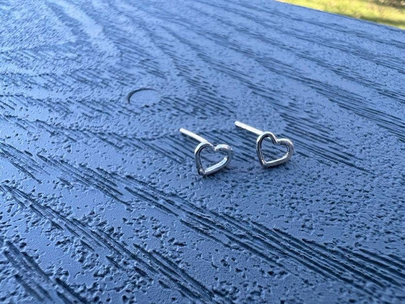 Thumbnail: Two silver heart shaped earrings lay on a blue wooden surface.