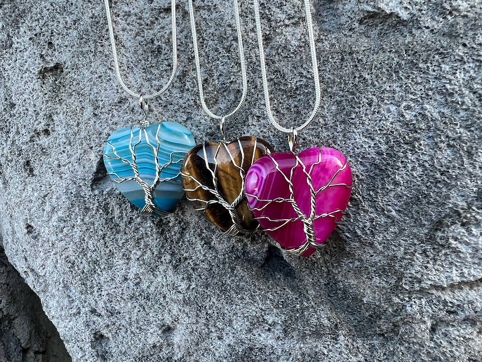 Thumbnail: Three heart-shaped gemstone necklaces displayed on a gray stone surface.