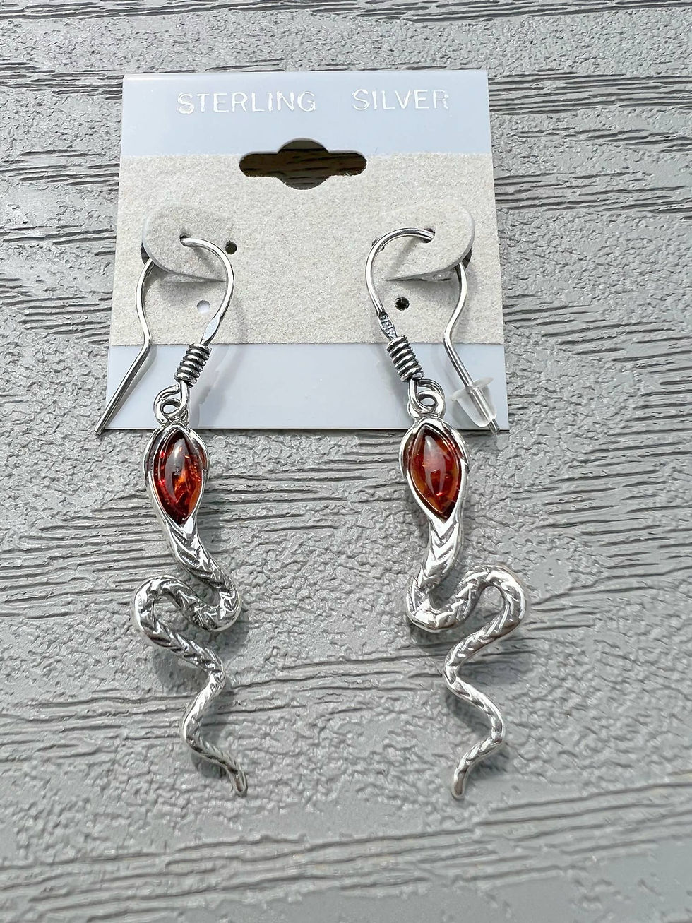 Silver snake earrings on an 'STUDIO 31' tag, red stone detail, jewelry.
