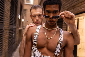2 male fashion models showing off a stylish vest and a trendy pair of sunglasses.