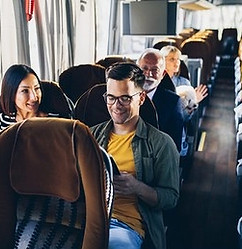 Passengers, including a man looking at his phone and a woman smiling, sitting on a bus.