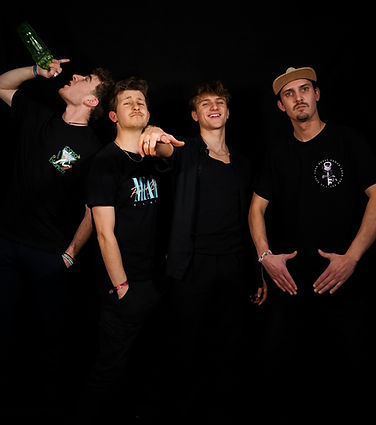 Lustiges Gruppenbild der Band. Felix trinkt aus einer Flasche Gin, Michi, Konsti und Luca schauen lustig in die Kamera
