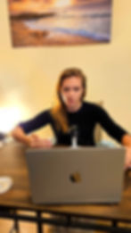 žena v černém svetru před žloutou zdí, která přednáší na webináři u laptobu macbook air