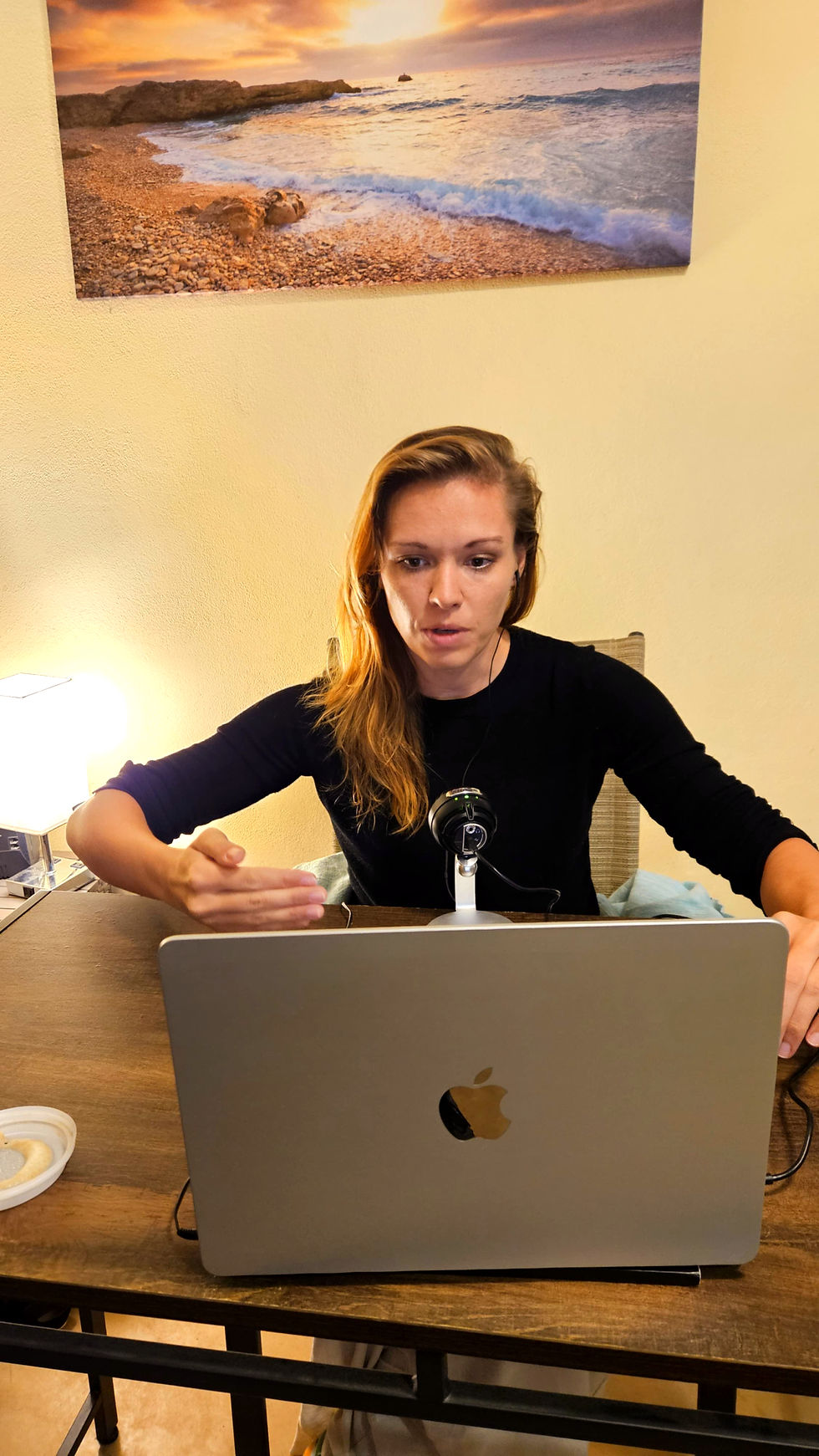 žena v černém svetru před žloutou zdí, která přednáší na webináři u laptobu macbook air