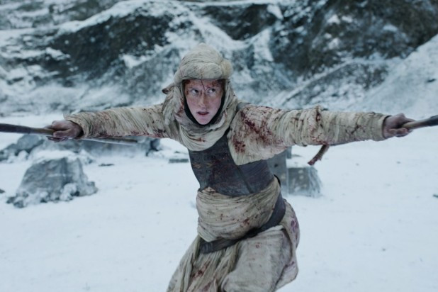 Actor Magdalena Sittova as Tigraine, a pregnant woman dressed in tan Aiel clothing with leather armor, holding two spears out to either side of her in a defensive position.