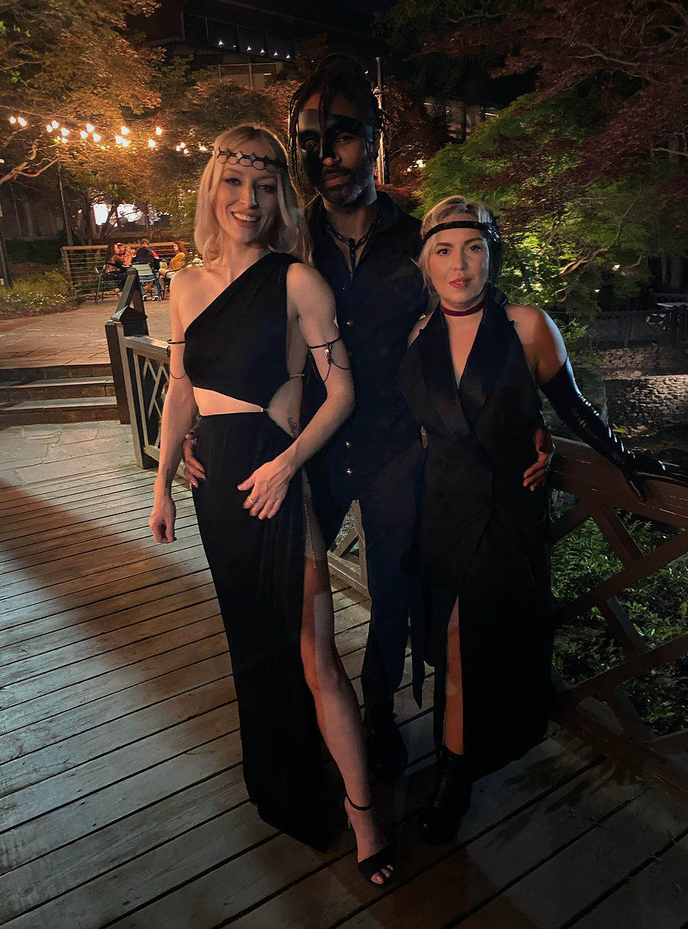 Tigraine, Collin, and Jay dressed in formal black attire with black accessories. Collin wears a black mask on half his face. 