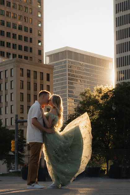 Engagement photography of a couple kissing as the sunset bursts through the buildings in downtown Detroit Hart Plaza