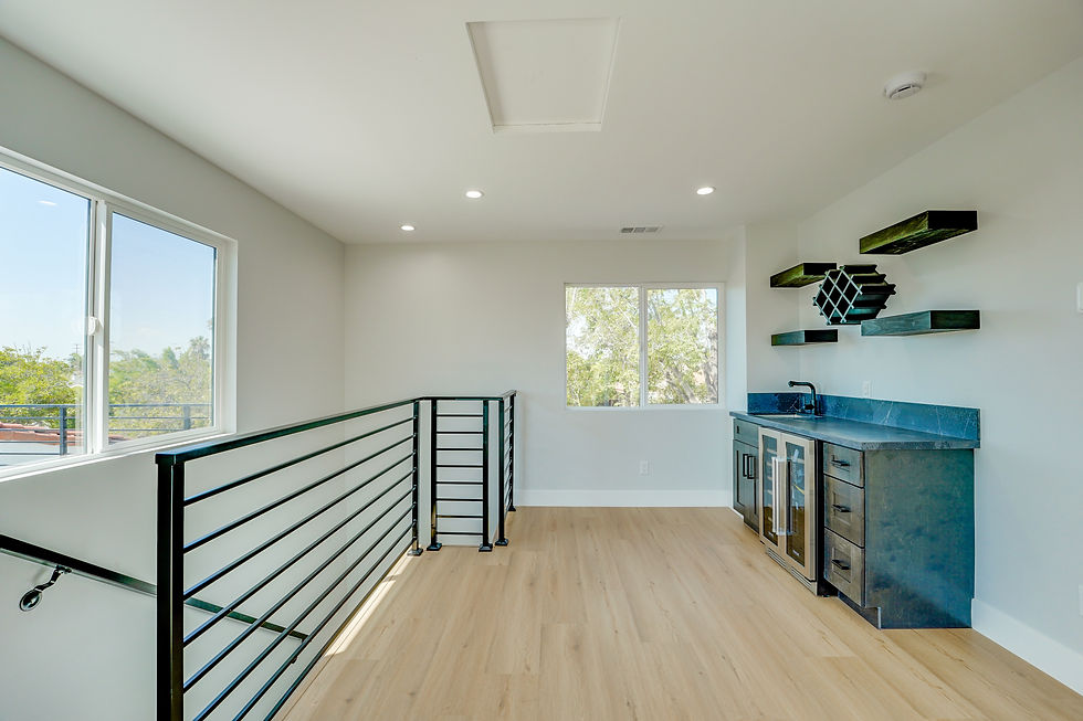 Bright upper-level loft space with hardwood floors, modern railing, and a blue cabinet wet bar.