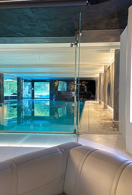 Vista della piscina interna da una zona relax con divano, ambientazione elegante e luminosa.