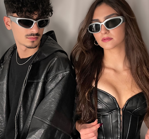 A stylish man and woman wearing futuristic sunglasses and sleek all-black outfits, exuding a bold, edgy aesthetic. The man pa