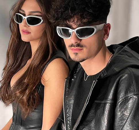 A stylish man and woman wearing futuristic sunglasses and sleek all-black outfits, exuding a bold, edgy aesthetic. The man pa