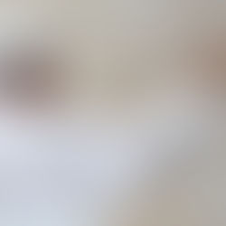 Pope in white robes and skullcap raises a hand in a greeting gesture against a plain beige background.