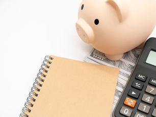 Piggy bank beside a calculator, notebook, and dollar bills on a white background, suggesting budgeting and savings.