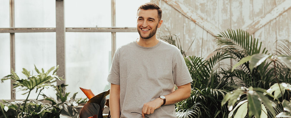 man in grey tshirt smiling while standing among plants