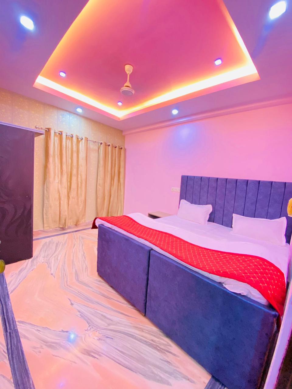 Vibrant bedroom with a striking blue bed frame and red accents, set against a pink wall. The room features a unique ceiling d