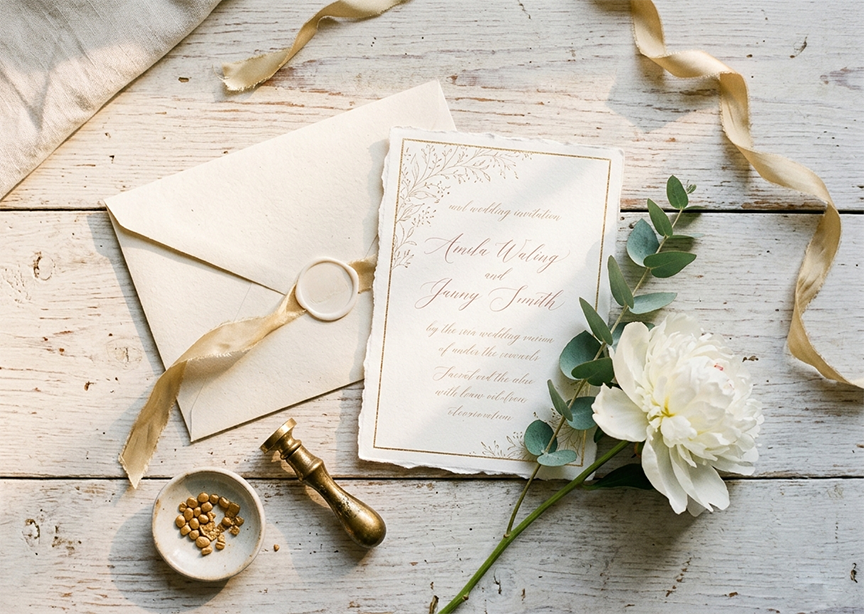 Elegant wedding invitation, envelope, wax seal, ribbon, and white flower on rustic wood; names Amie Wang and Jenny Smith visible.