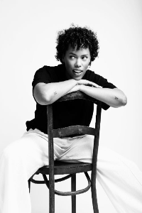 Ashley pose pour ralfagram sur une chaise en bois avec un pantalon Jacquemus et un tshirt noir la photo en noir et blanc a été réalisée dans le studio personnel de ralfagram à La Hulpe