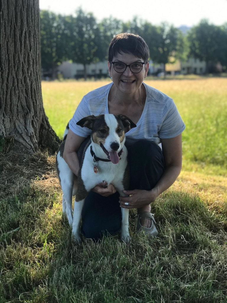 Frau mit Hund in der Hocke auf einer Wiese