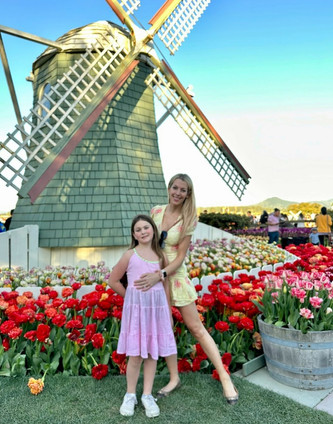 Woman and girl standing in front of windmill surrounded by tulips