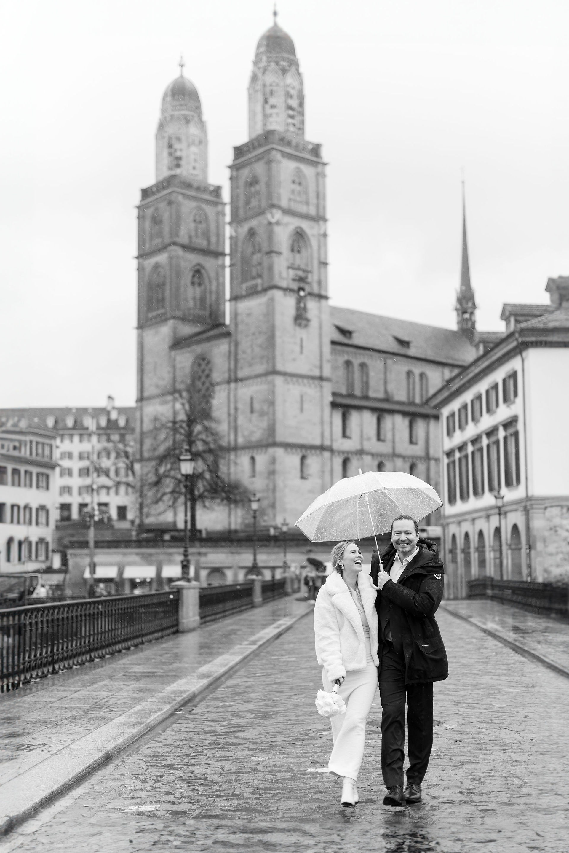 Winter civil wedding in Zurich, Switzerland. Couple holds umbrella and laughs in the rain.