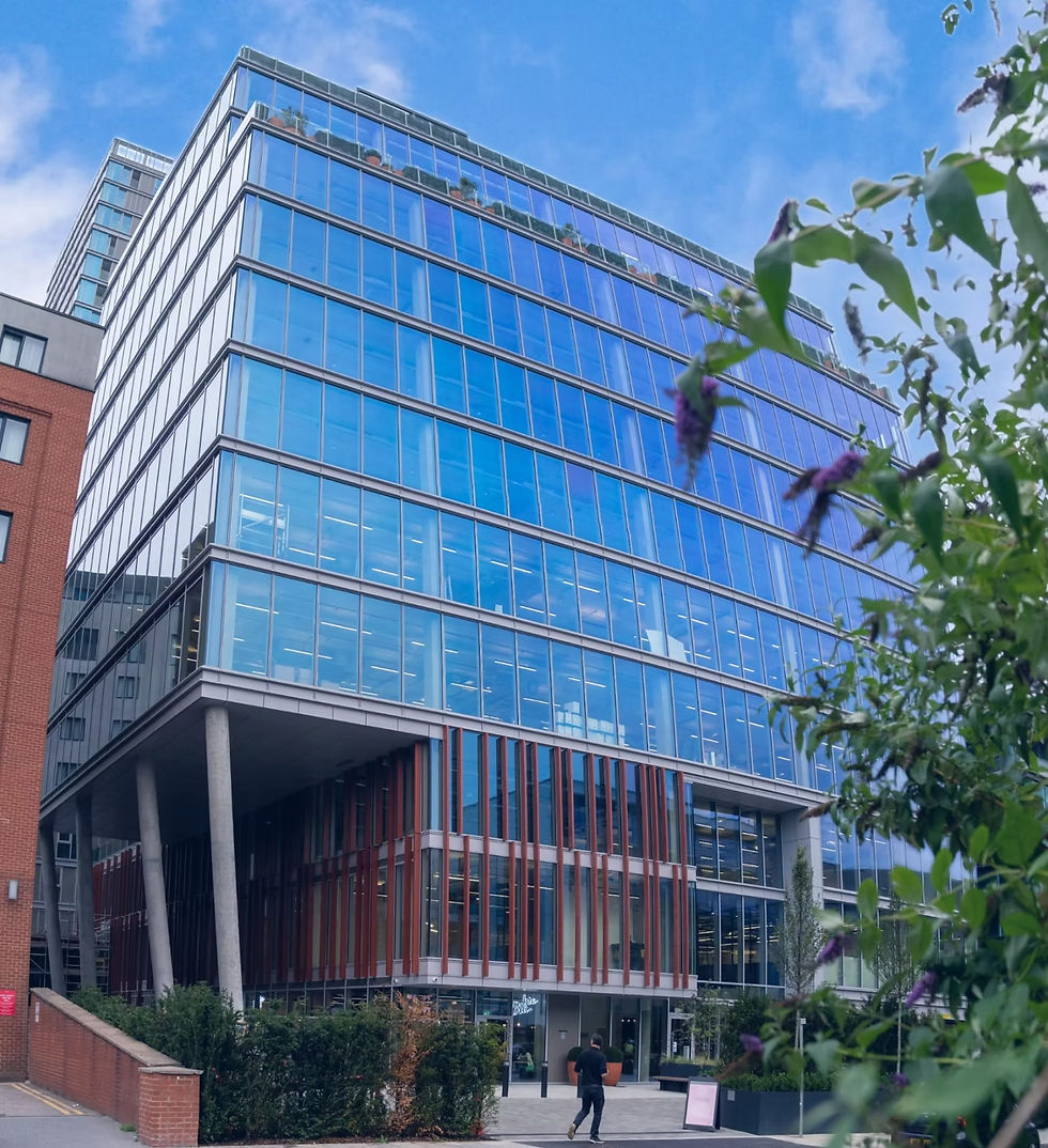 Modern glass office building with blue sky reflections and green foliage.