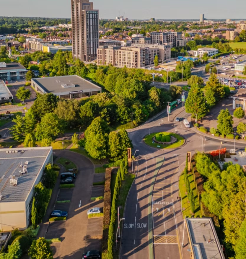 Aerial view of urban area featuring roads, buildings, trees, and a roundabout.