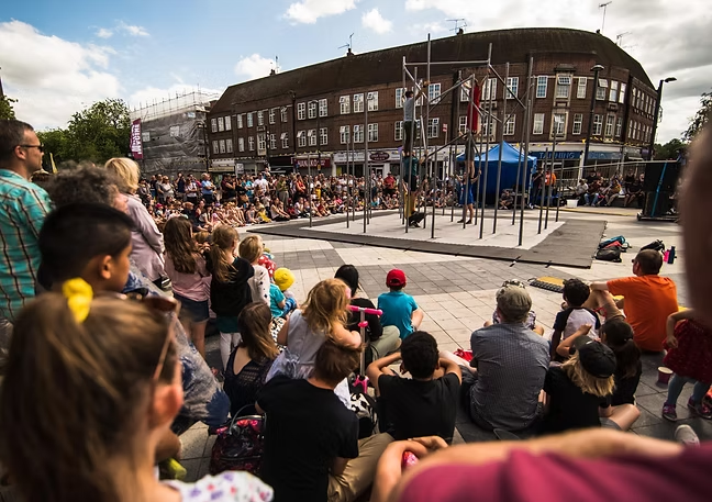 Acrobats perform on bars for a large crowd at an outdoor event.