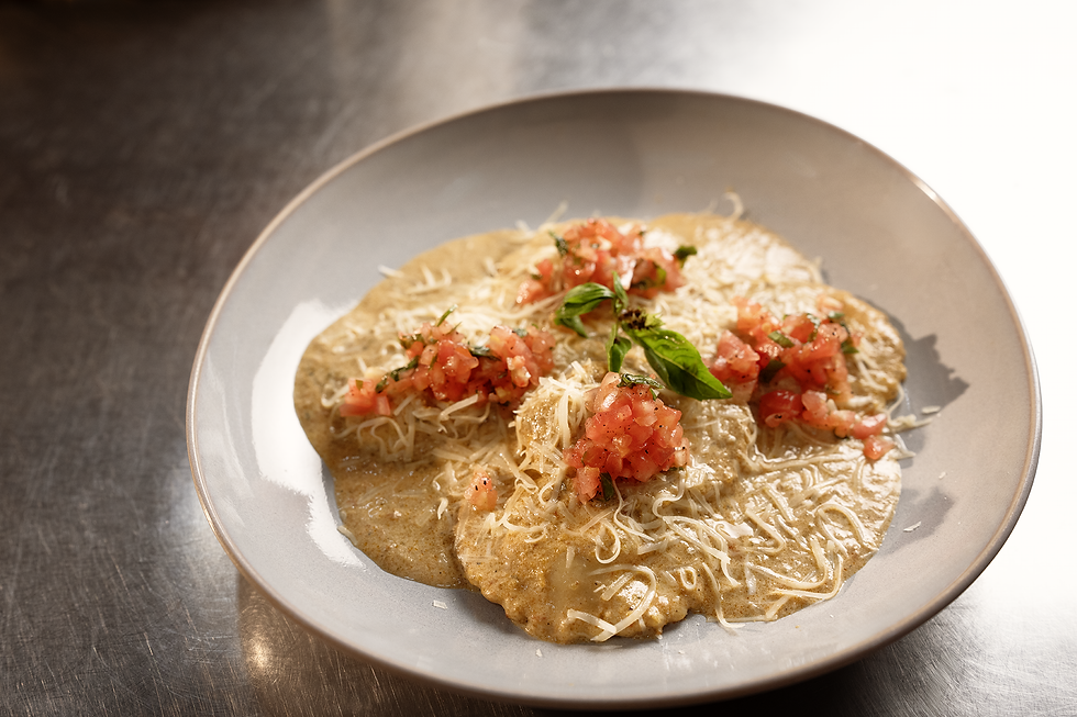 Preparación gratinada con queso fundido, pico de gallo fresco y hojas de albahaca en plato blanco.