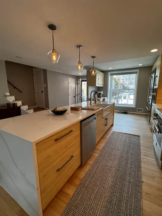Prep side of the island with oak drawers, an integrated dishwasher and a farmhouse sink, under three glass globe pendants.