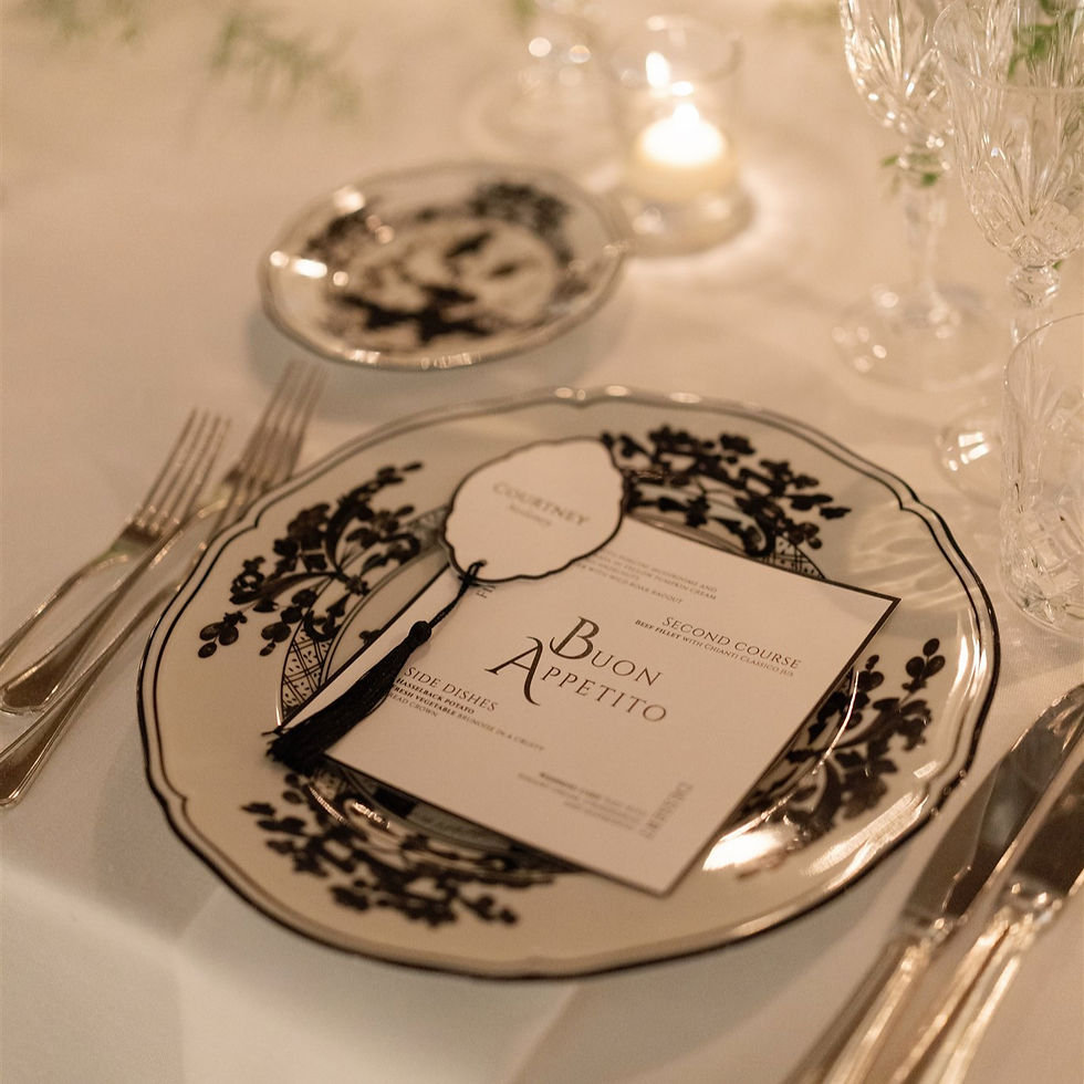Elegant wedding table setting with floral-patterned plates, menu titled "Buon Appetito," silverware, and crystal glasses on a white tablecloth.
