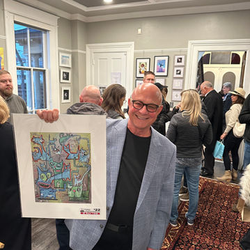 Man holds art piece at an event, smiling. Community event in the venue.