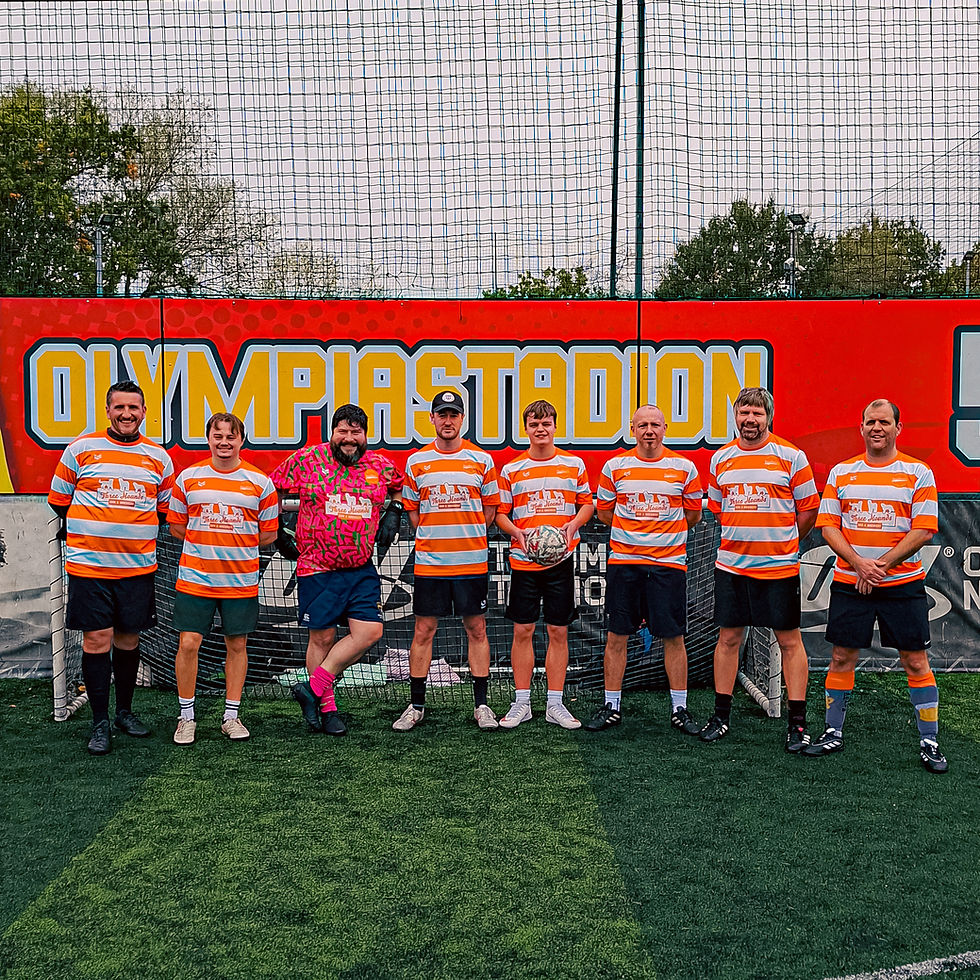 Seven men in orange-and-white soccer jerseys pose on a turf field in front of a red OLYMPIASTADION sign, smiling.