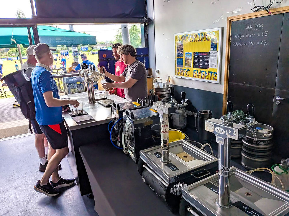 People at an outdoor bar; one person serves drinks from taps. Signs show "Upcoming BRFC Events" and beer types. Sunny and social setting.