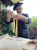 Italian chef Claudio in a chef hat holding up fresh noodles during a pasta making demo in Burchio, Italy