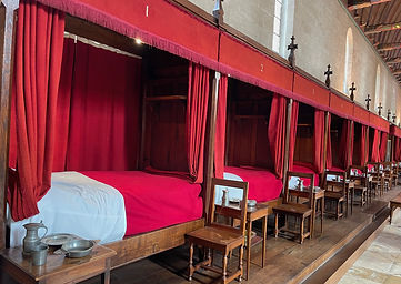 A row of red hospital beds and curtains line the wall inside Hotel Dieu in Beaune, France