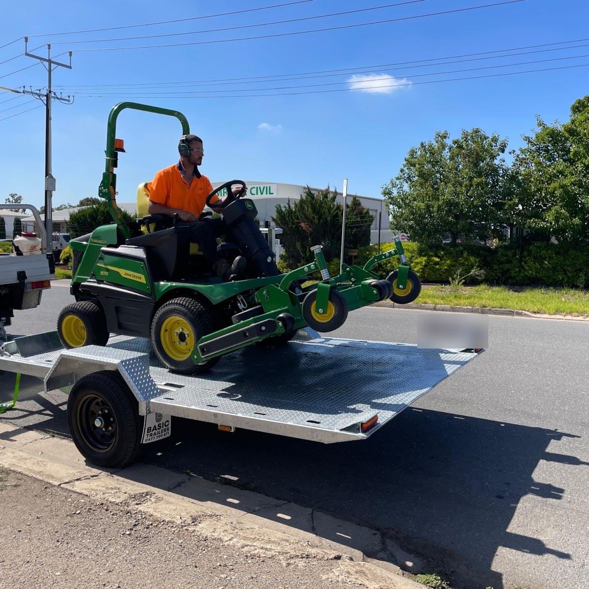 Tree and Grounds operator driving a John Deere front deck ride-on mower onto a trailer