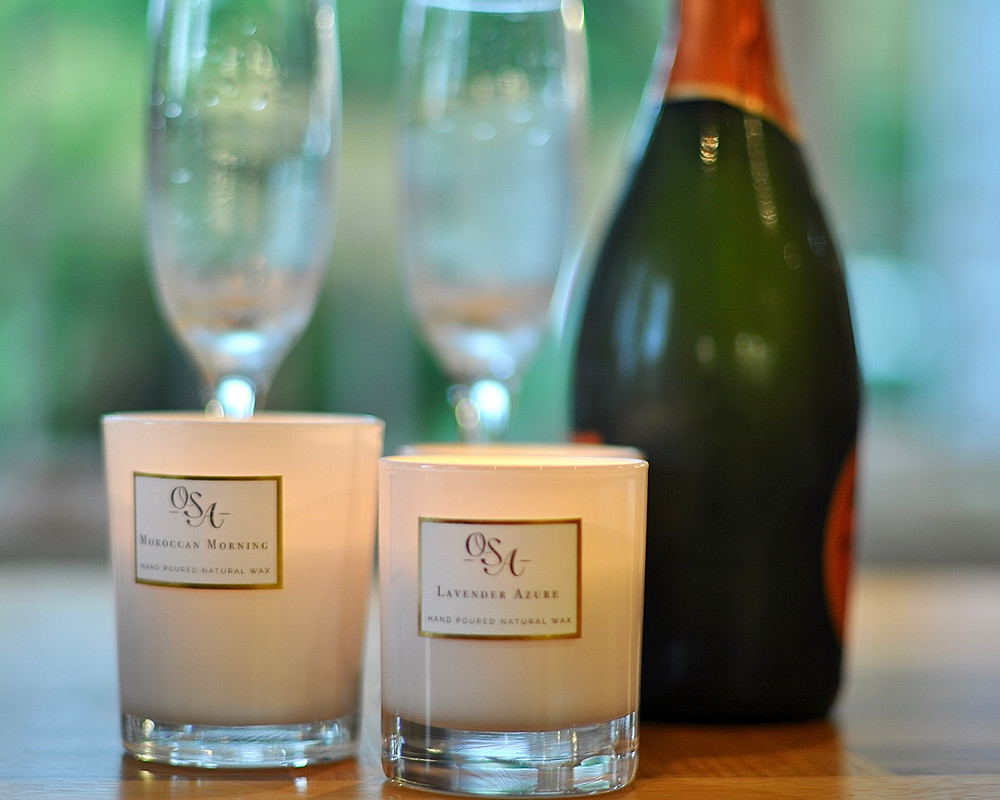 Two candles burning in the foreground with a champagne bottle in the background