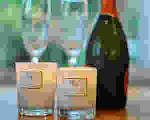 Two candles burning in the foreground with a champagne bottle in the background