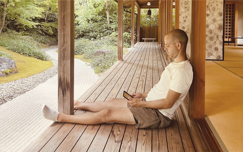A man reading on his e-reader in a building that is part of a Japanese garden.