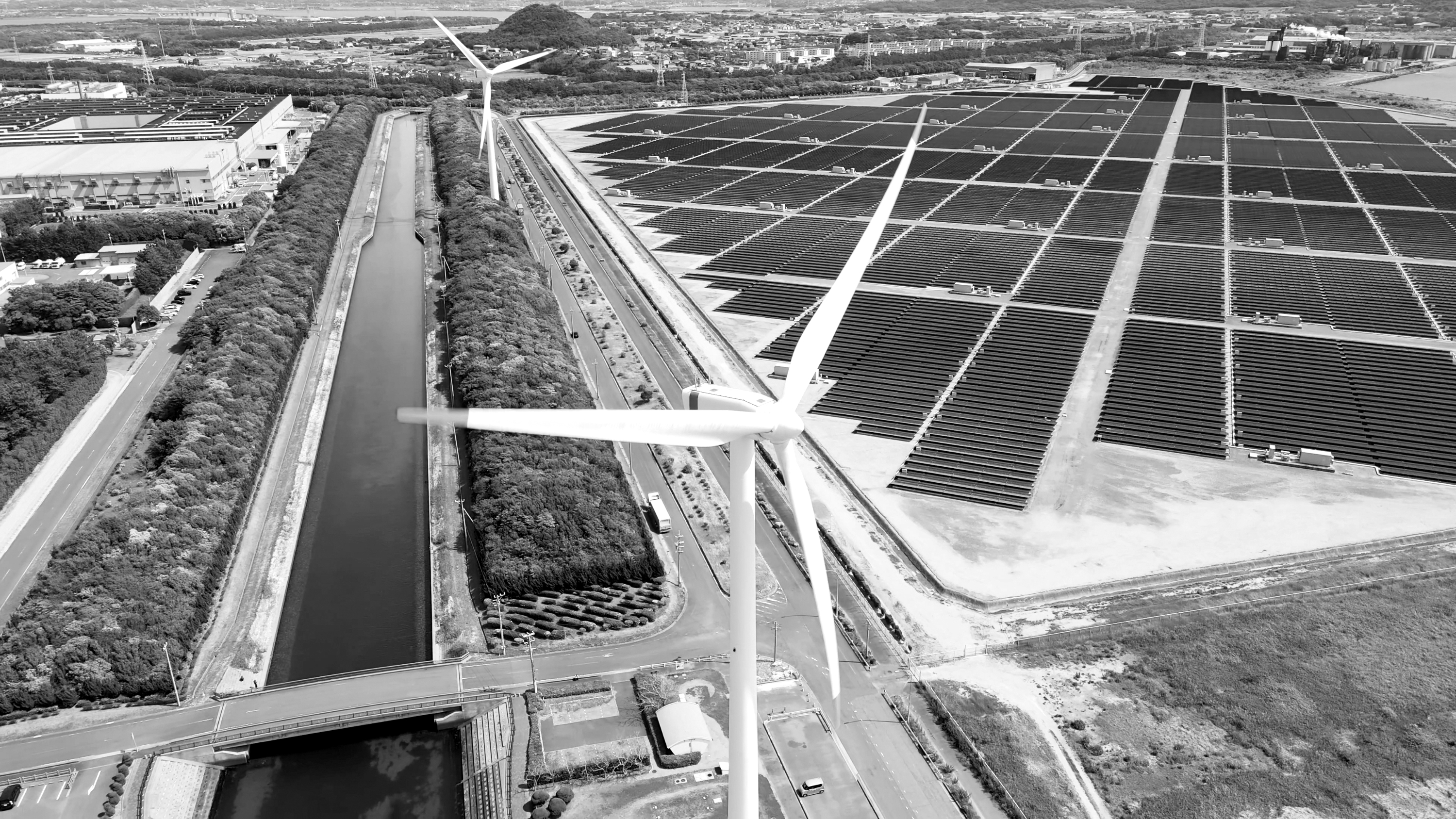 Schwarz-Weiß-Luftaufnahme von Windenergieanlagen neben einem großen Solarpark und einem Kanal.