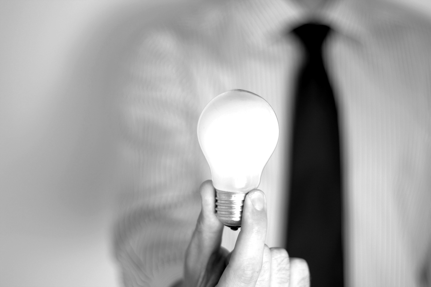 A person in a shirt and tie holds a light bulb against a bright background. Focus on the bulb, with stripes in the foreground.