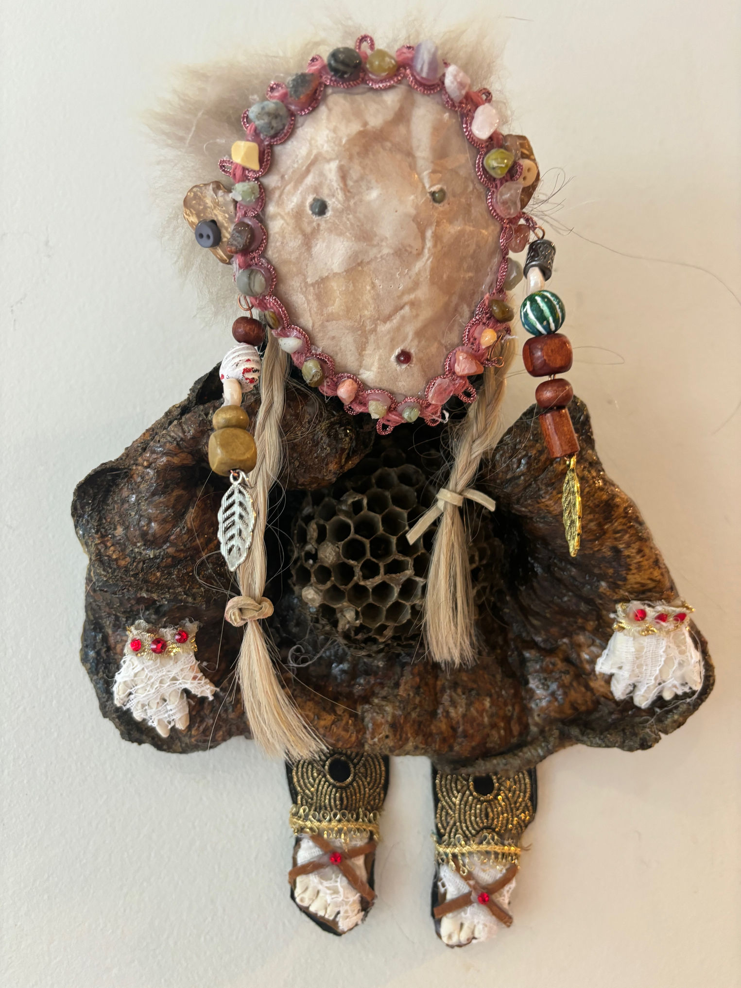 a female figure, the body made from tree fungus and the face a paper maché mask is mounted on a painted stretched canvas.
