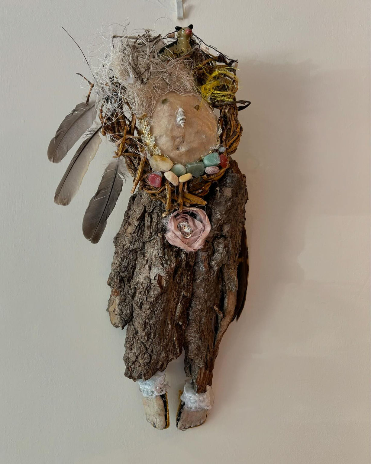A female figure with a driftwood body and a paper maché mask for a face is mounted on a painted stretched canvas