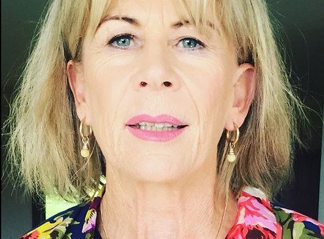 Photo of Keiley Hunter, with shoulder length blonde hair, pink lipstick gold drop earing and a colourful shirt