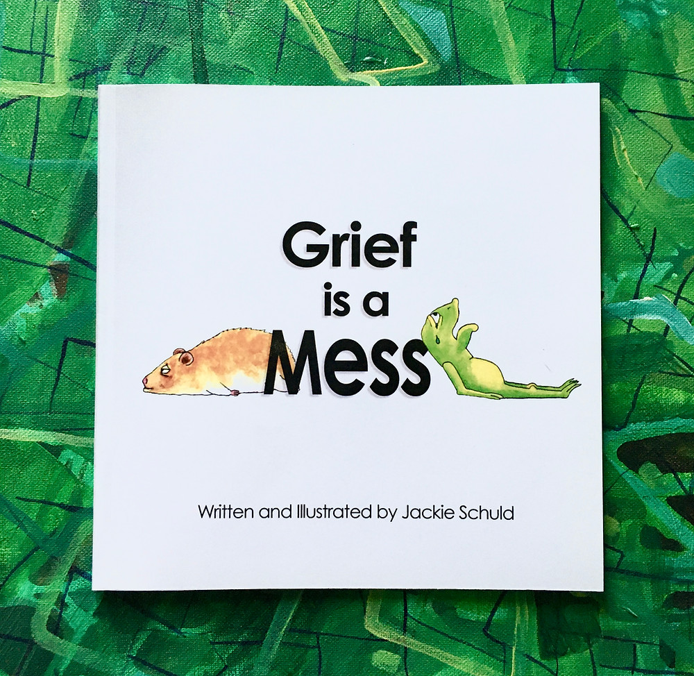 Picture of the book "Grief is a Mess" by Art Therapist Jackie Schuld. The book is placed on a green abstract painting. The book cover contains a hamster and frog that are very sad.