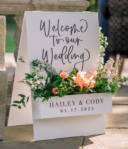 Custom wedding welcome sign reading "Welcome to our Wedding" in script with fresh floral accents