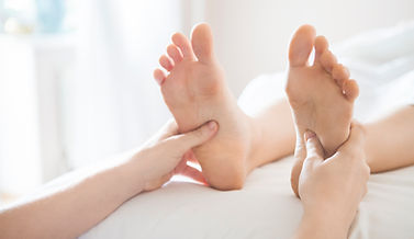 A person is receiving a foot reflexology massage, with the therapist's hands applying gentle pressure to specific points on the soles of the feet. The client's face shows a sense of relaxation and comfort as the therapist works on different reflex zones to promote overall well-being and balance in the body. The scene reflects the therapeutic nature of foot reflexology, aimed at enhancing relaxation and supporting health benefits through the feet.
