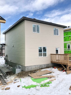 New two-story house, beige siding, wooden deck, snowy construction site.